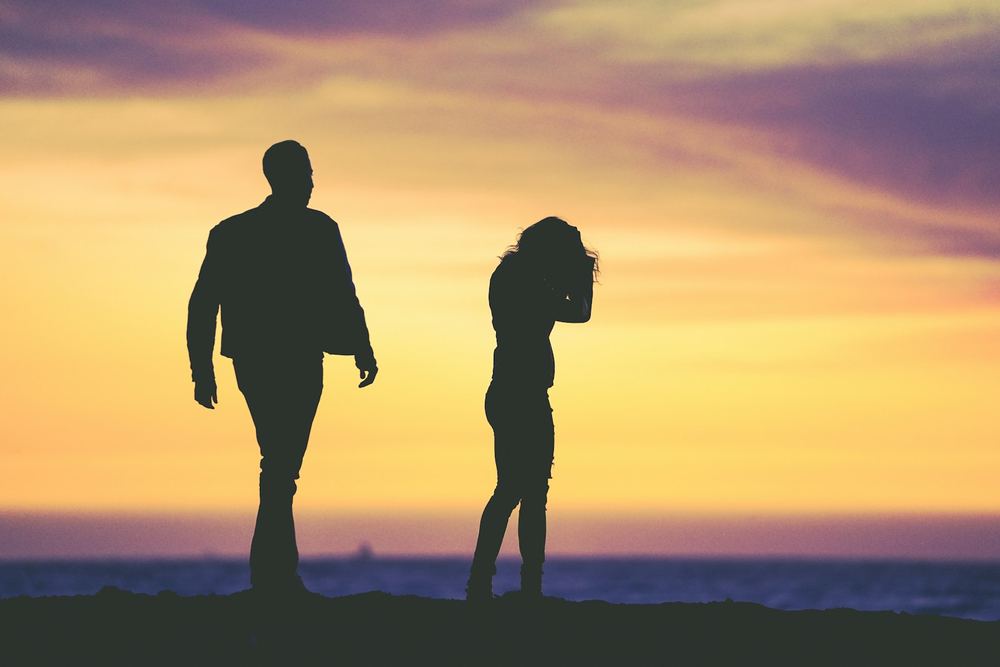 Silhueta de um casal caminhando em direções opostas ao pôr do sol