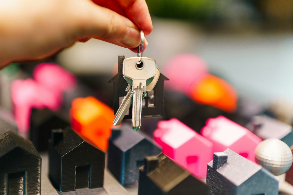 Mão segurando chaves de casa sobre casas em miniatura