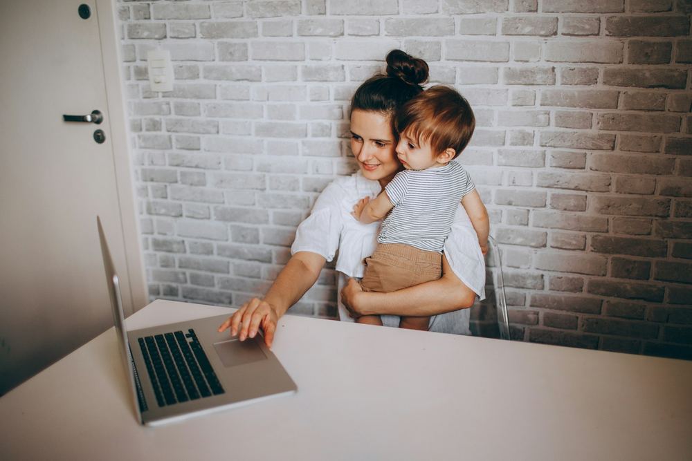 Mãe com o filho pequeno no colo, trabalhando no notebook